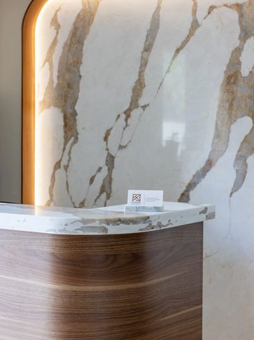 Modern reception desk with marble top and wood paneling against a marble wall.
