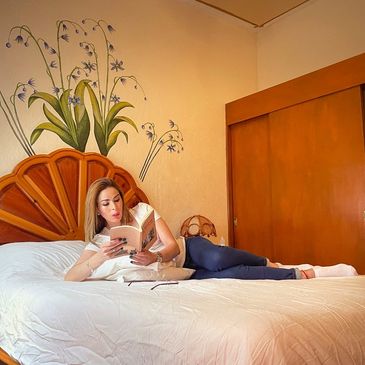 Woman reading a book while lying on a bed with floral wall art.