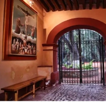 Interior view of a chapel with a crucifix painting and iron gate.
