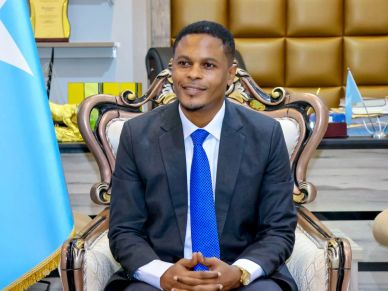 Man in suit sitting on an ornate chair with a blue flag.