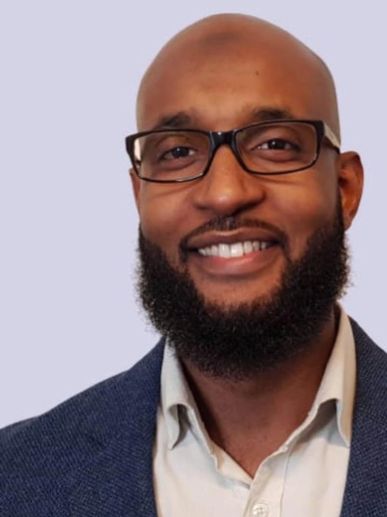 Smiling man with glasses and beard wearing a suit.