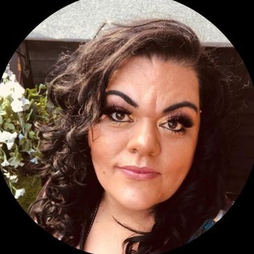 A close‑up portrait of a person with dark curly hair and gold eyeshadow. They are wearing  eyeliner