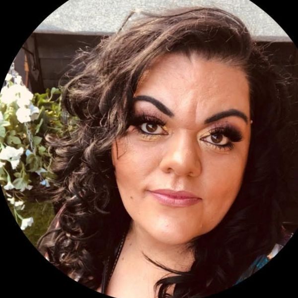 Woman with curly hair and striking makeup looks confidently at the camera.