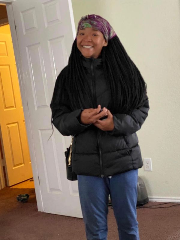 Smiling woman in black jacket and purple headscarf.