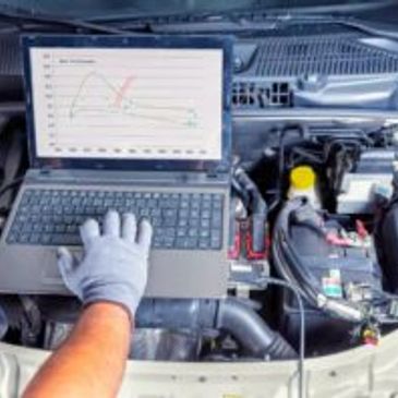 Mechanic diagnosing car engine with laptop.
