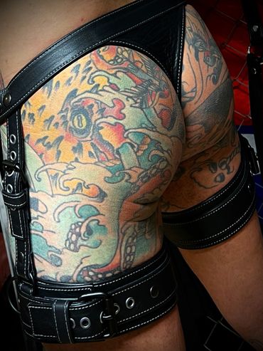 Colorful tattoos on legs with black leather harness and straps.