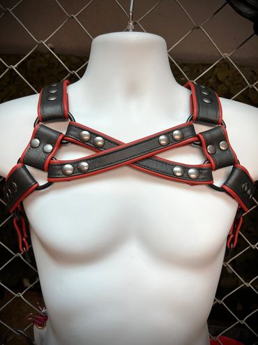 Black and red leather chest harness with metal studs on a white mannequin.