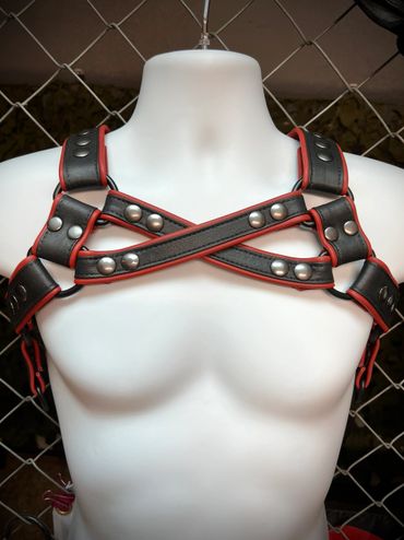 Black and red leather chest harness with metal studs on a white mannequin.