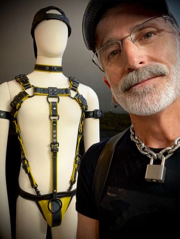 Man with a chain lock necklace poses next to a mannequin in leather harness.