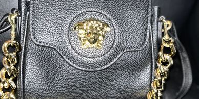 Close-up of a black leather Versace bag with gold Medusa emblem and chain detail.