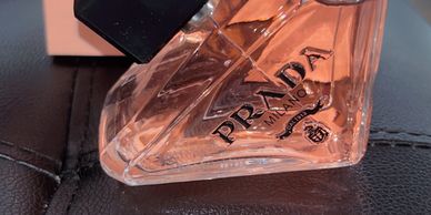 Close-up of a Prada perfume bottle with pink liquid on a black surface.