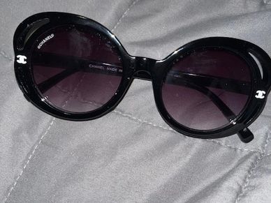 Black Chanel sunglasses with round frames on a gray surface.