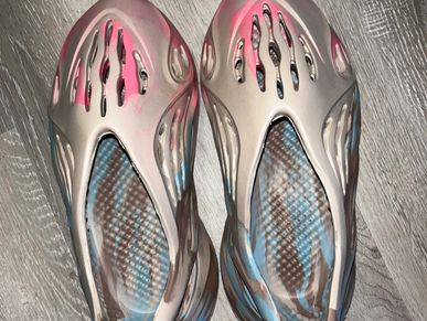 A pair of beige foam slip-on shoes with cut-out designs and colorful insoles.
