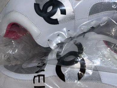 Close-up of white Chanel sneakers with black logo inside plastic wrapping.