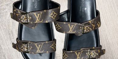 Pair of Louis Vuitton sandals with monogram straps on wooden floor.