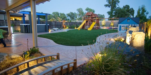 Backyard landscape design with concrete, pergola, artificial turf, landscape lighting, plants, etc