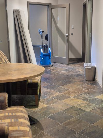 A small room with tiled floor, chairs, table, and an open door showing cleaning equipment.