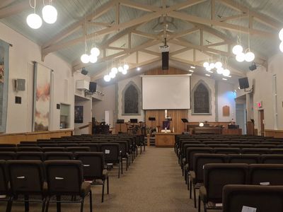 Interior of a well-lit church with rows of chairs and a stage at the front.