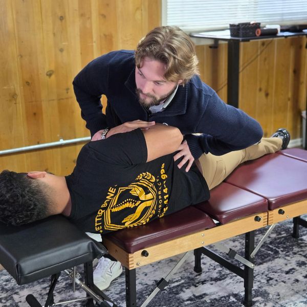 Chiropractor adjusting a patient's back on a treatment table in a wood-paneled room.