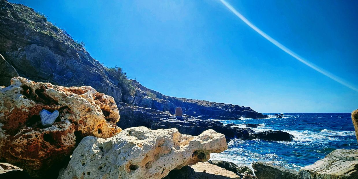 Rocky seaside under clear blue sky with a heart-shaped stone.
