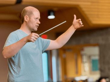 Man conducting music with a baton indoors.