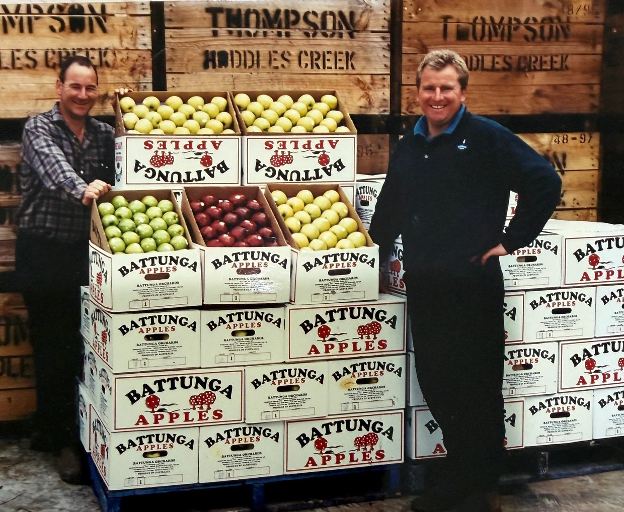 Two men stand by stacked boxes of Battunga apples.