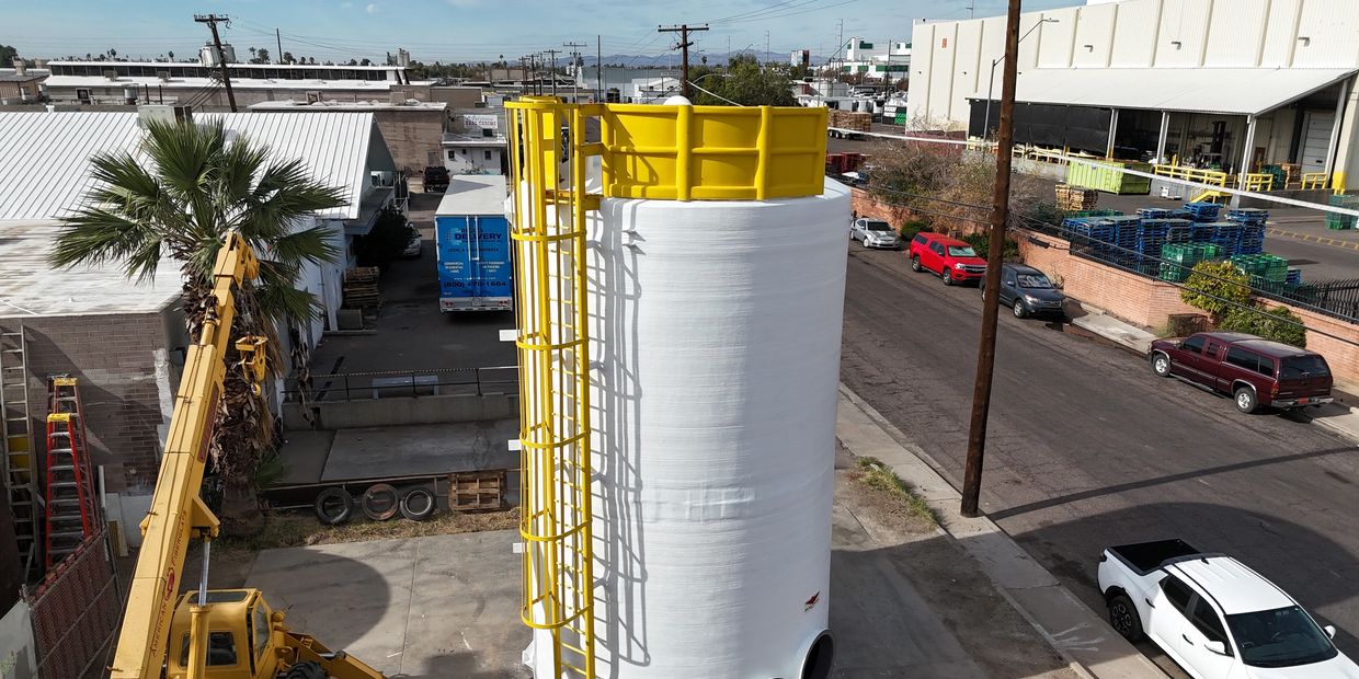 Large white industrial tank with yellow safety railing and ladder in an urban area.