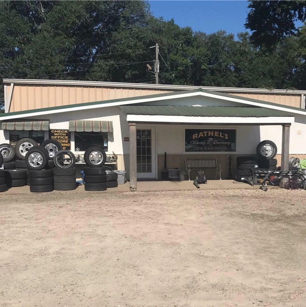A tire and towing service shop with tires stacked outside and a sign that reads Rathel's Towing & Recovery.