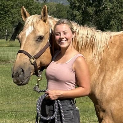 Young woman smiling beside a palomino horse outdoors.