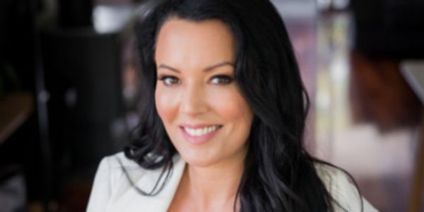 Smiling woman with long black hair wearing a white blazer.