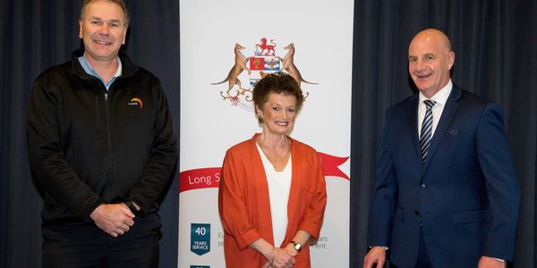 Three professionals pose in front of a banner with a coat of arms.