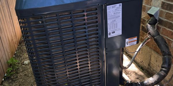 Outdoor air conditioning unit installed beside a brick wall.