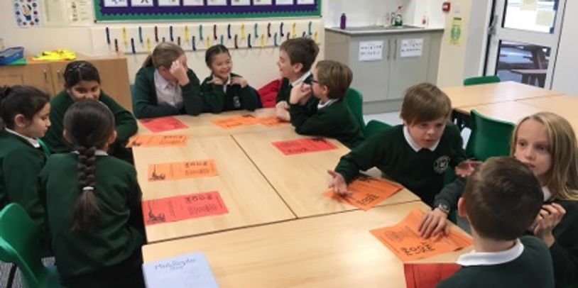 Children in school uniforms engaged in group activity around tables.