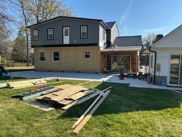 Two-story house under renovation with construction materials in the yard.