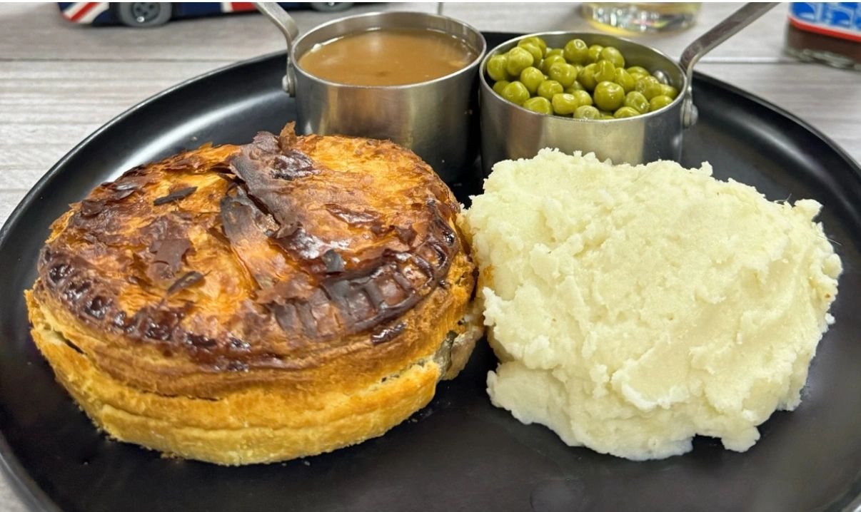 A meat pie served with mashed potatoes, peas, and gravy on a black plate.