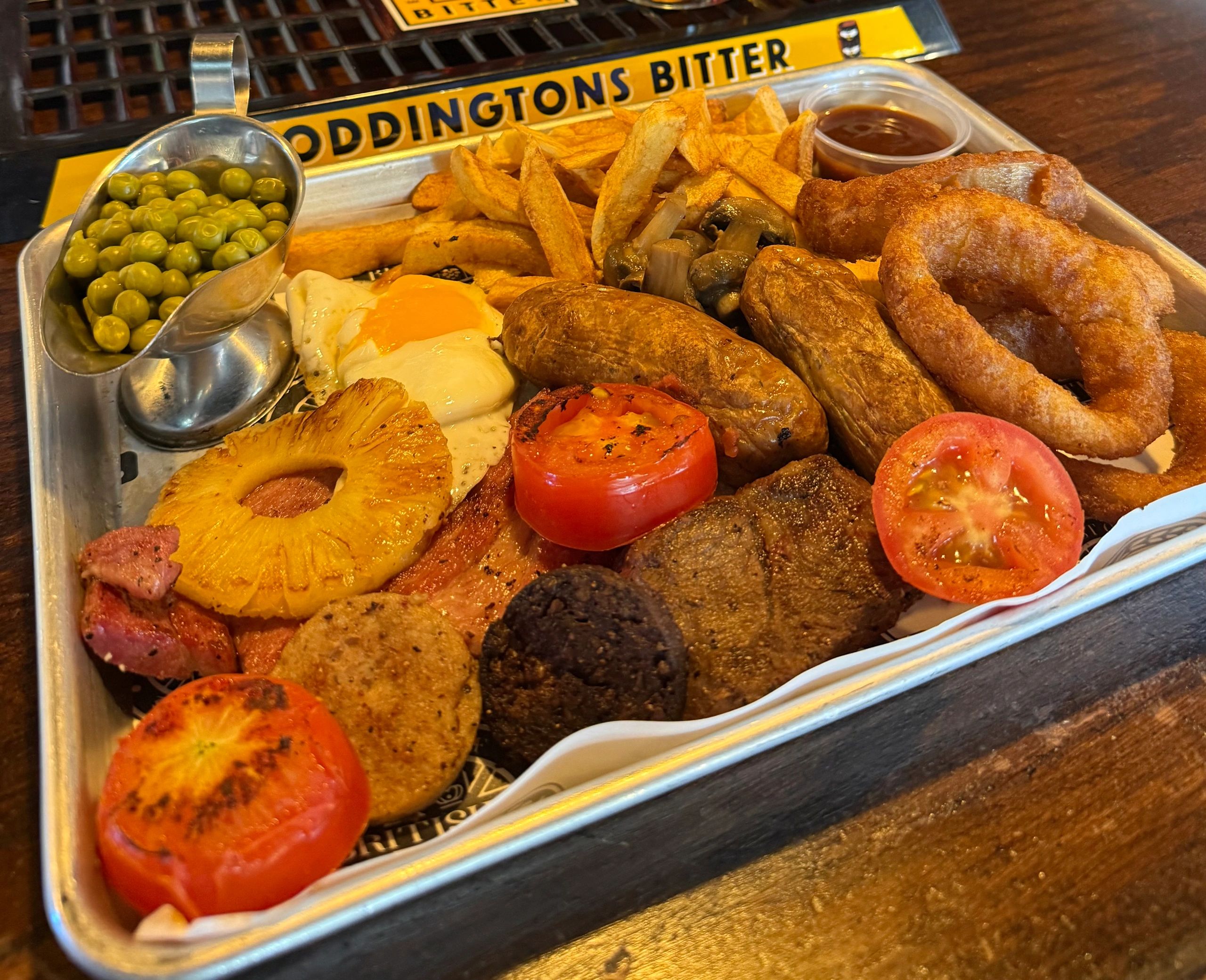 A hearty English breakfast with peas, eggs, tomato, sausages, and fries.