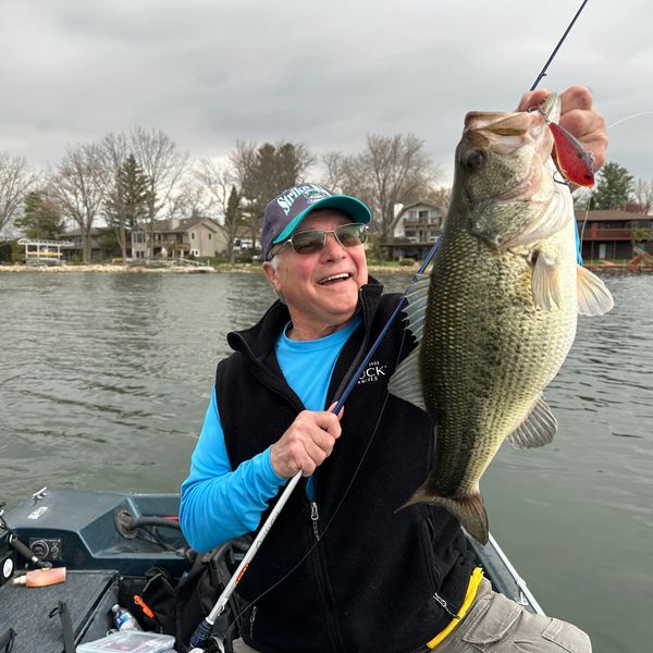 Man proudly holding a large fish on a boat in a lake.