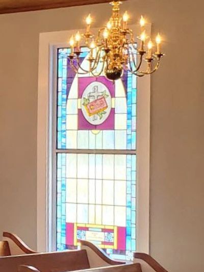 Stained glass window with a chandelier above in a church.