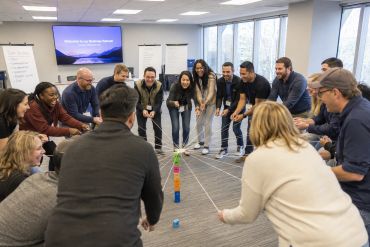 Team building activity with participants holding strings connected to blocks.