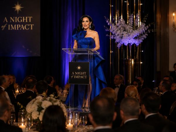 Woman in a blue dress speaks at 'A Night of Impact' event.