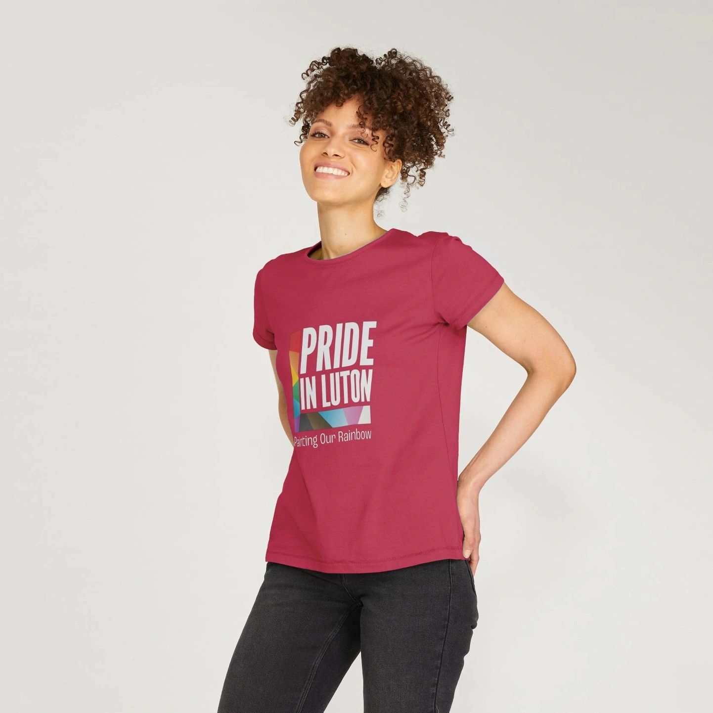 A smiling woman wearing a red tee with the light Pride In Luton logo printed on the front.