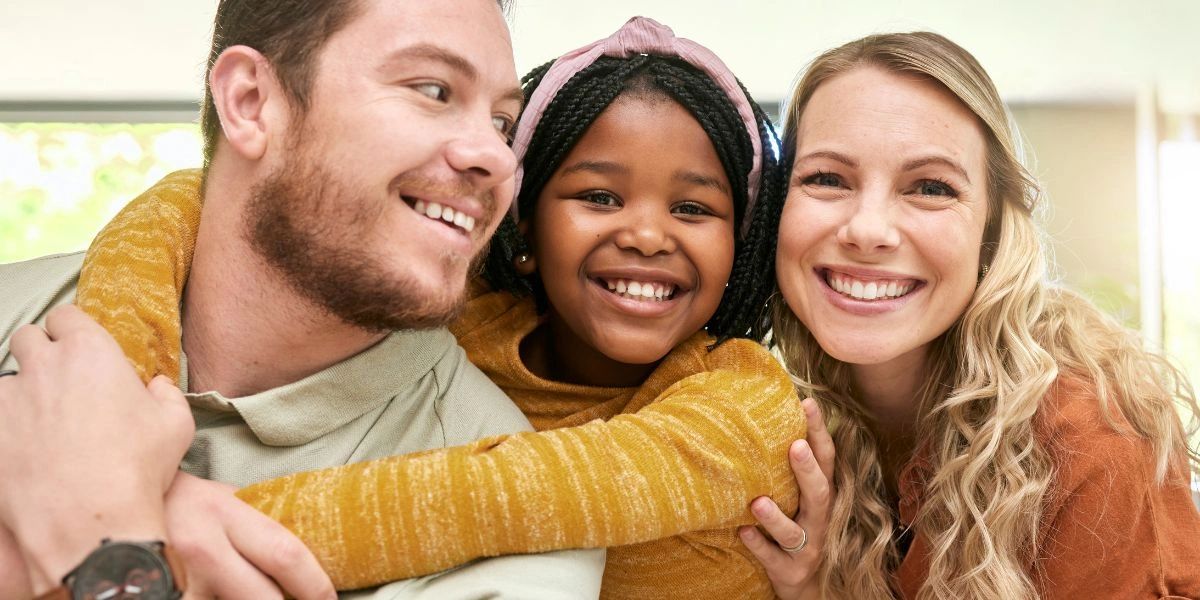 Three people smiling warmly, embracing each other in a close group hug.