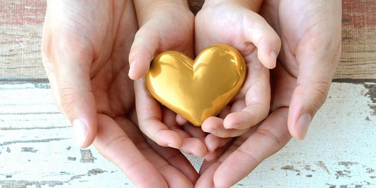 Adult and child hands holding a golden heart together.