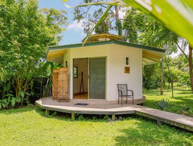 Small octagonal cabin with porch in lush green garden.