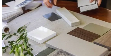 Hands examining various countertop and tile samples on a table.