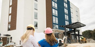 Two construction workers plan in front of a modern building under construction.