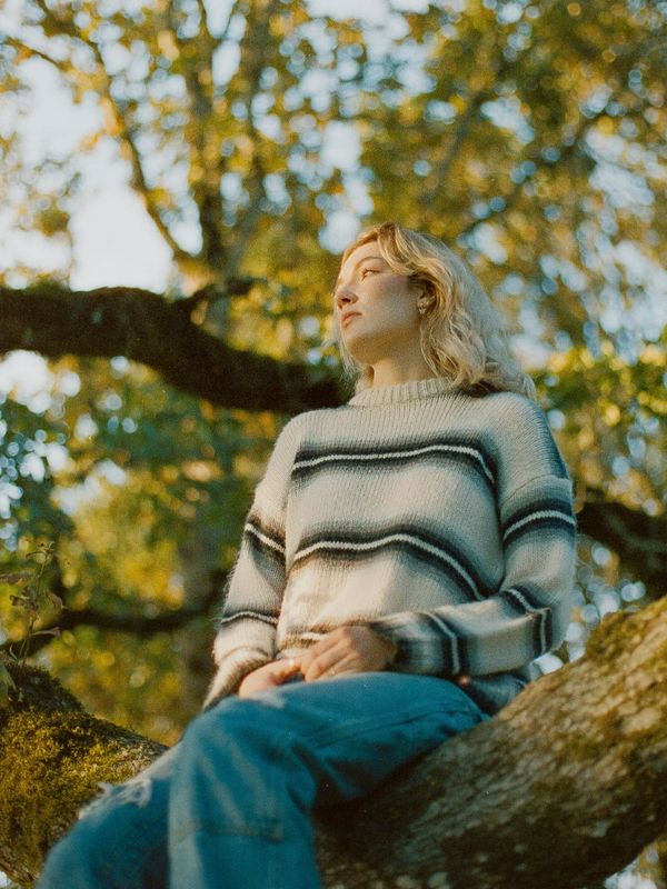Young woman sitting on a tree branch outdoors.