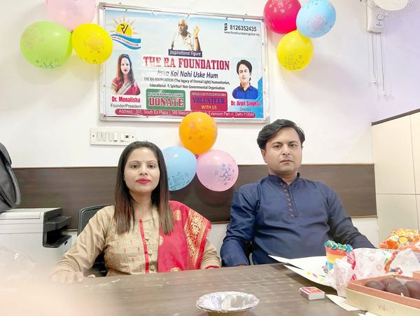 Two individuals seated in an office decorated with colorful balloons and a foundation banner.