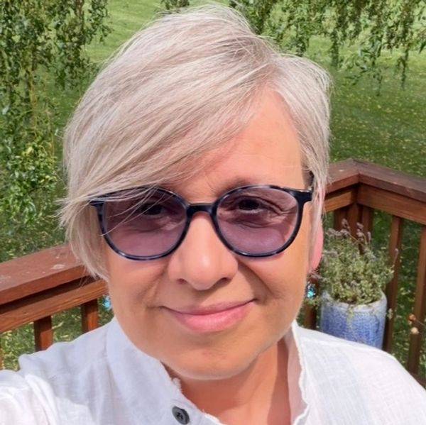 Kathrin Winter Owner and Treating Therapist smiling and standing on deck with tree and flower pots i
