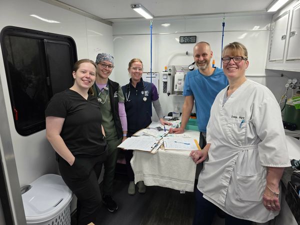 A group of five medical professionals smiling inside a clinic room.